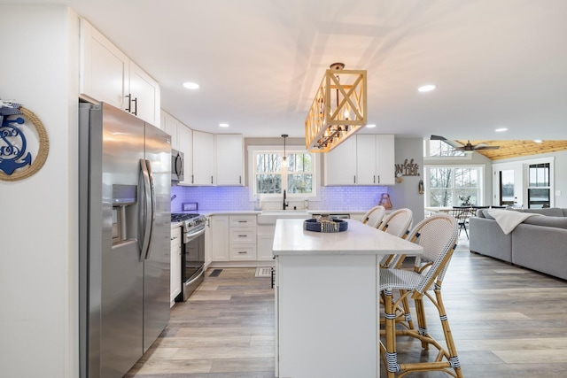 kitchen featuring a kitchen bar, white cabinetry, hanging light fixtures, and appliances with stainless steel finishes