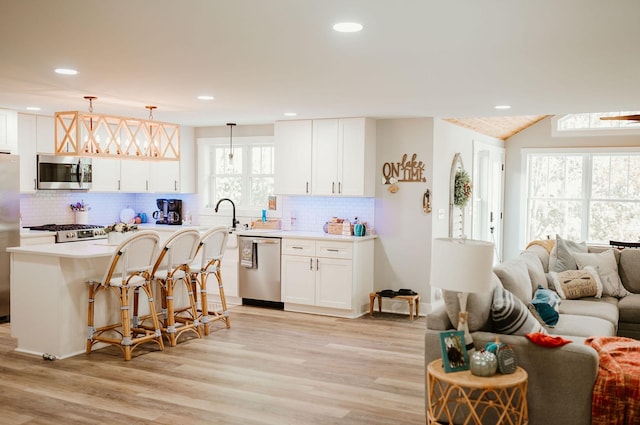 kitchen featuring a kitchen breakfast bar, a wealth of natural light, stainless steel appliances, white cabinets, and hanging light fixtures