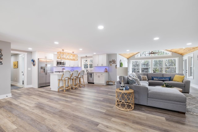 living area with light wood finished floors, baseboards, recessed lighting, vaulted ceiling, and a notable chandelier