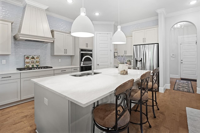 kitchen with pendant lighting, premium range hood, crown molding, an island with sink, and appliances with stainless steel finishes