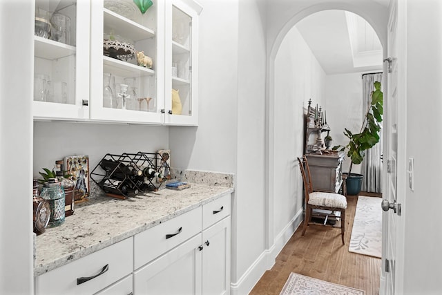 bar featuring light hardwood / wood-style floors, white cabinetry, and light stone counters