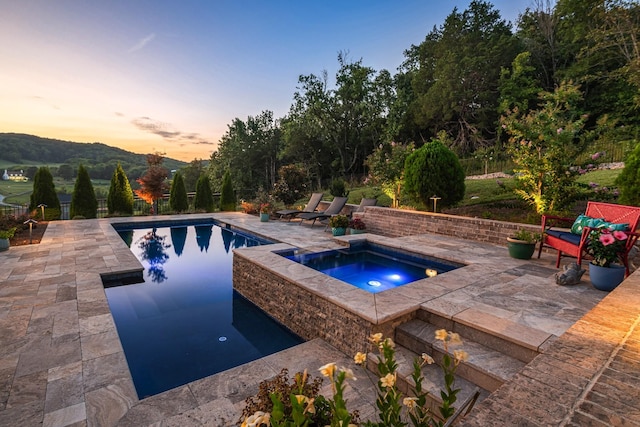 pool at dusk with an in ground hot tub, a mountain view, and a patio