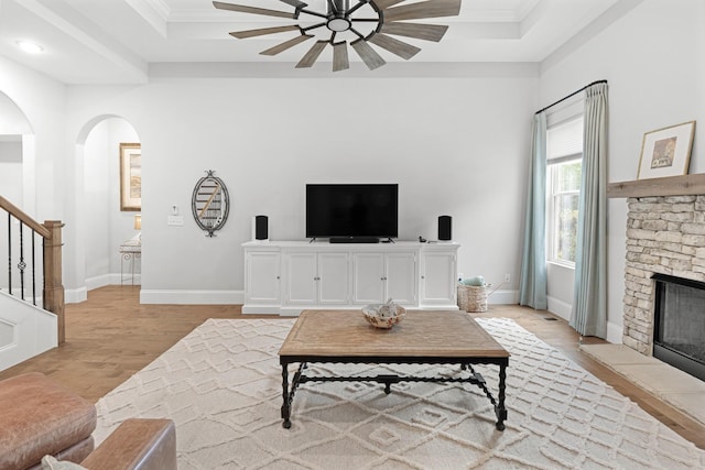 living room with a raised ceiling, a fireplace, ornamental molding, and light hardwood / wood-style flooring