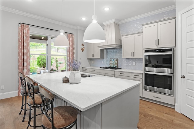 kitchen featuring decorative light fixtures, gas stovetop, stainless steel double oven, and an island with sink