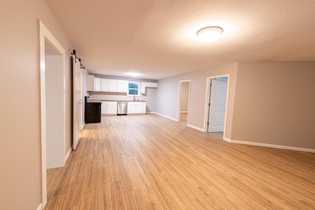 unfurnished living room featuring a textured ceiling, light hardwood / wood-style floors, a barn door, and sink