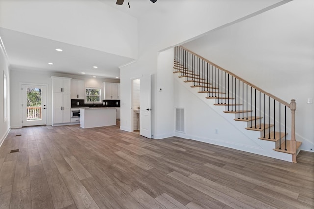 unfurnished living room featuring hardwood / wood-style flooring, ceiling fan, crown molding, and sink