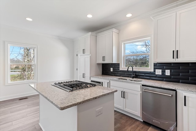 kitchen with white cabinetry, sink, a center island, light stone counters, and appliances with stainless steel finishes