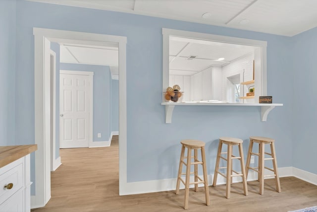 kitchen featuring baseboards, light wood-type flooring, white cabinetry, and a kitchen breakfast bar