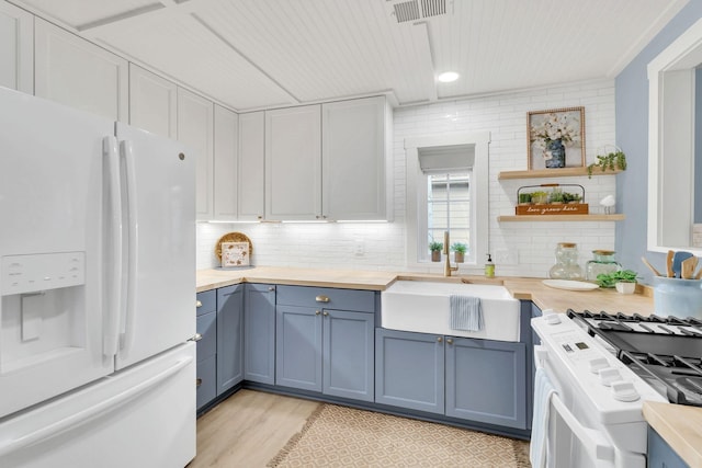 kitchen with blue cabinetry, visible vents, backsplash, a sink, and white appliances