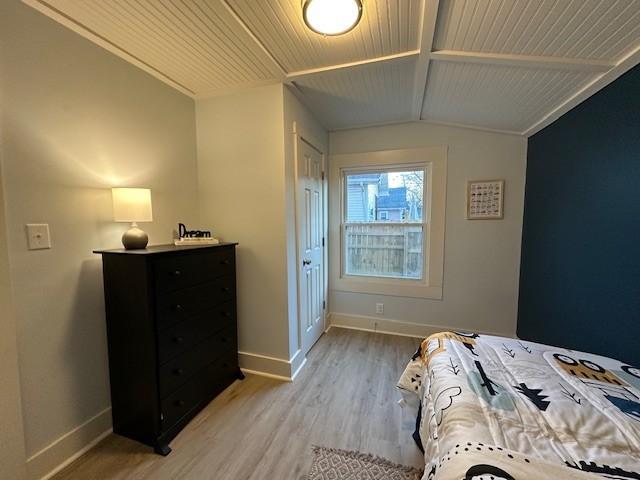 bedroom with lofted ceiling with beams, light wood-style floors, and baseboards