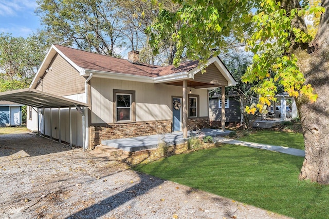 view of front of house featuring gravel driveway, a chimney, a detached carport, a front yard, and stone siding