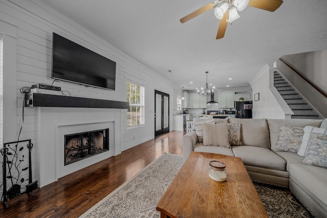 living room with dark hardwood / wood-style flooring, ceiling fan with notable chandelier, a large fireplace, wooden walls, and crown molding