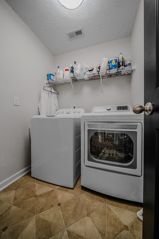 laundry area featuring washer and clothes dryer, tile patterned flooring, and a textured ceiling