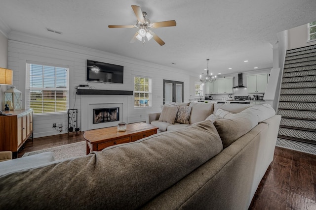 living room with ornamental molding, a textured ceiling, ceiling fan with notable chandelier, dark hardwood / wood-style floors, and wood walls