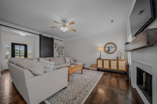 living room featuring a barn door, ceiling fan, dark hardwood / wood-style flooring, and ornamental molding