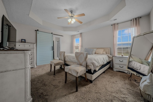 carpeted bedroom featuring ceiling fan, a barn door, a raised ceiling, and multiple windows