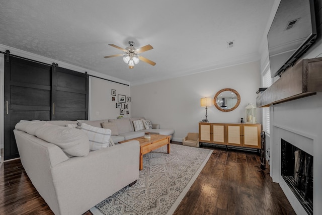 living room with dark hardwood / wood-style flooring, a barn door, ceiling fan, and ornamental molding