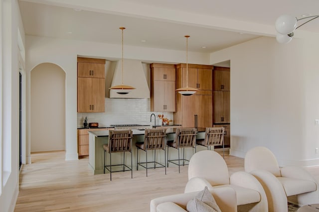 kitchen featuring hanging light fixtures, tasteful backsplash, a kitchen breakfast bar, a kitchen island with sink, and custom range hood