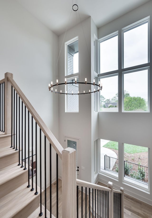 stairway with a chandelier, wood-type flooring, and a towering ceiling