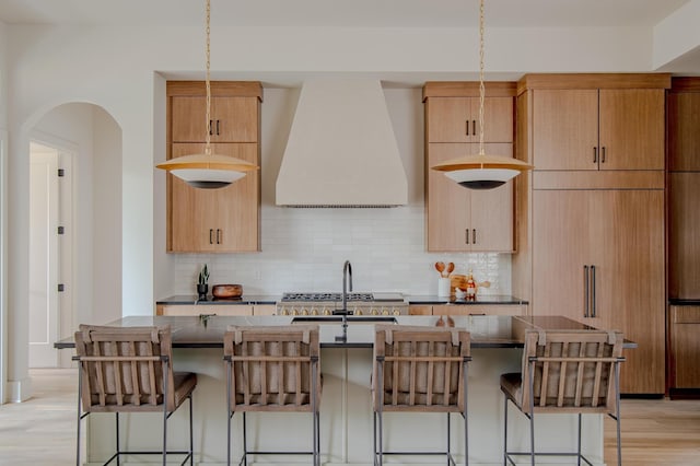 kitchen with hanging light fixtures, an island with sink, extractor fan, and tasteful backsplash