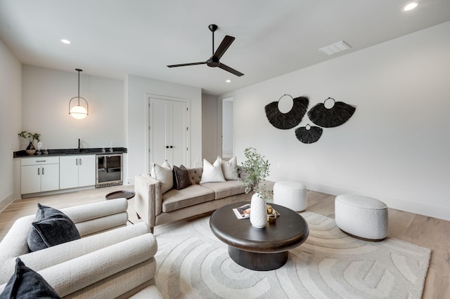 living room with ceiling fan, light hardwood / wood-style flooring, beverage cooler, and sink