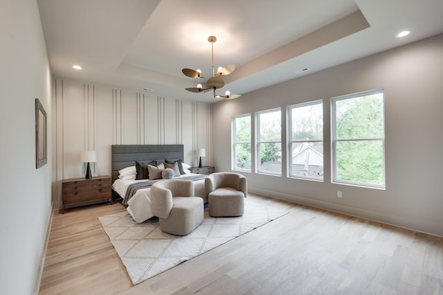 bedroom featuring light hardwood / wood-style floors, a raised ceiling, multiple windows, and an inviting chandelier