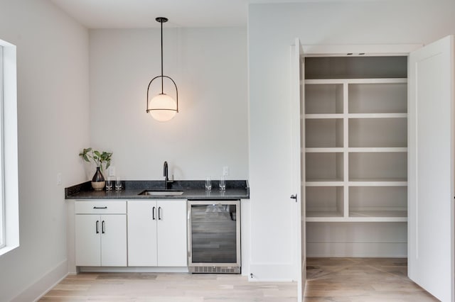 bar with pendant lighting, white cabinets, sink, light wood-type flooring, and beverage cooler