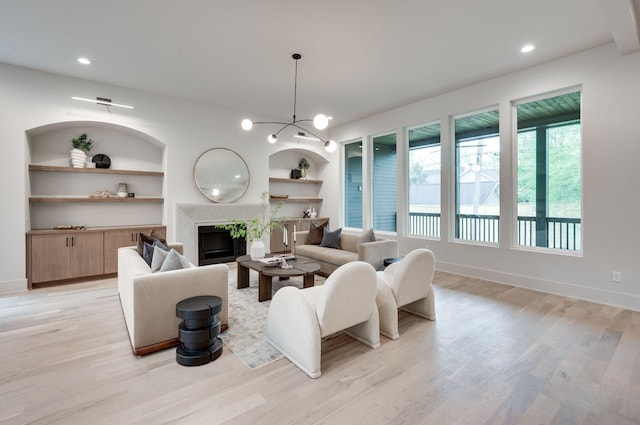 living room featuring plenty of natural light, light hardwood / wood-style floors, built in features, and a chandelier