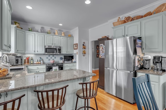 kitchen with crown molding, light hardwood / wood-style floors, light stone counters, and appliances with stainless steel finishes