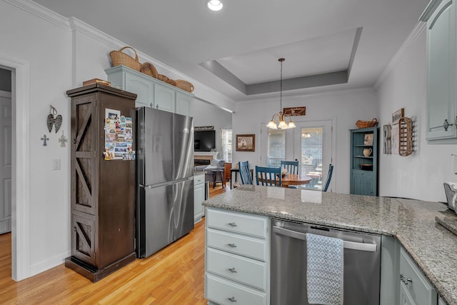 kitchen featuring stainless steel appliances, a raised ceiling, light stone counters, light hardwood / wood-style floors, and decorative light fixtures