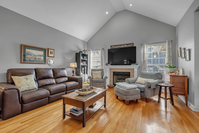 living room featuring a tiled fireplace, high vaulted ceiling, and light wood-type flooring