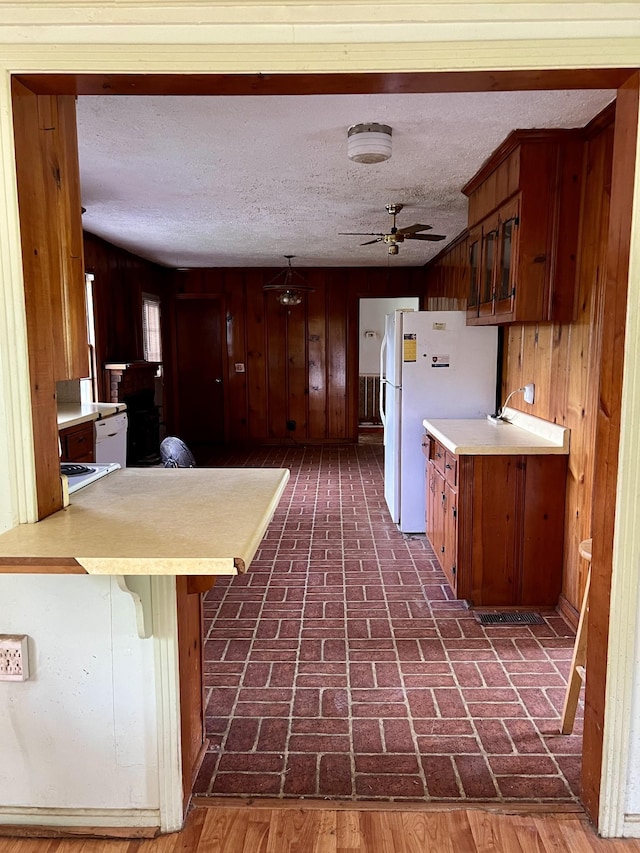 kitchen with kitchen peninsula, a kitchen breakfast bar, ceiling fan, wooden walls, and white refrigerator