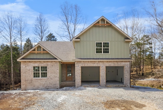 view of front facade featuring a garage, brick siding, a shingled roof, board and batten siding, and gravel driveway