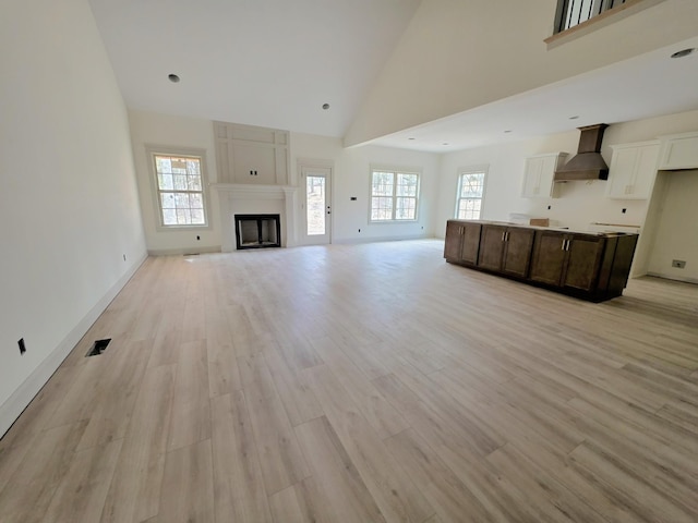 unfurnished living room featuring light wood-style floors, a fireplace, high vaulted ceiling, and a wealth of natural light