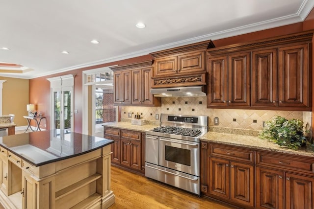 kitchen with a center island, stainless steel range with gas cooktop, light hardwood / wood-style flooring, ornamental molding, and range hood