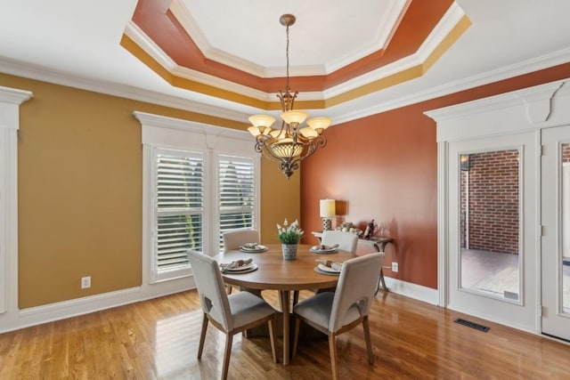 dining room with hardwood / wood-style floors, a tray ceiling, an inviting chandelier, and crown molding