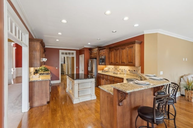 kitchen with sink, stainless steel appliances, light stone counters, kitchen peninsula, and a kitchen bar