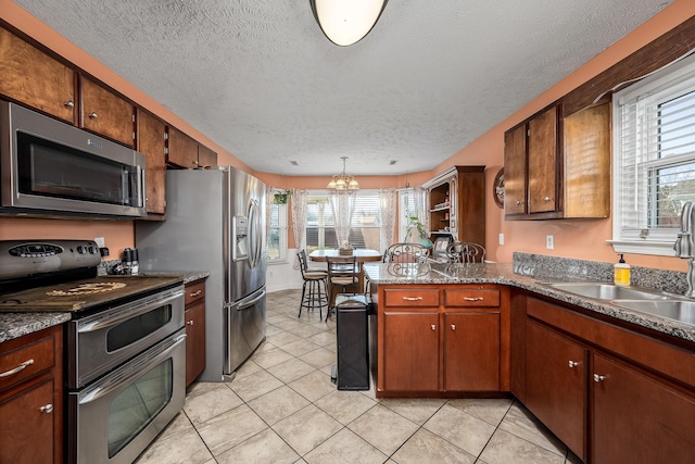 kitchen with kitchen peninsula, a textured ceiling, stainless steel appliances, pendant lighting, and light tile patterned floors