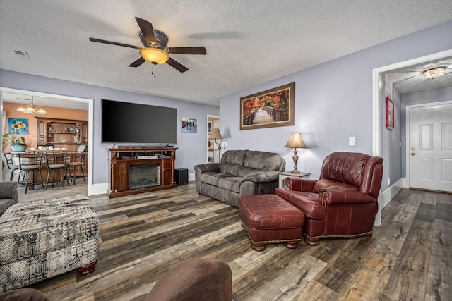 living room featuring ceiling fan with notable chandelier, a textured ceiling, and dark wood-type flooring