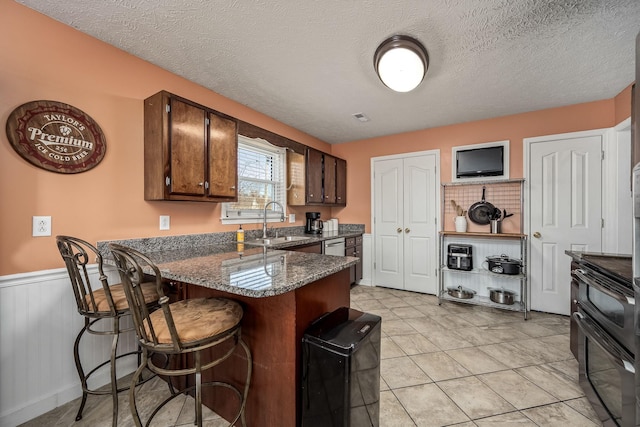 kitchen with dark stone counters, a textured ceiling, black range with electric cooktop, sink, and light tile patterned floors