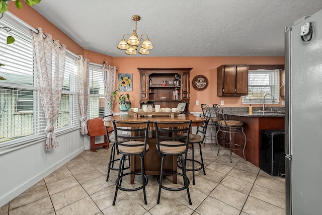 dining room with sink, light tile patterned floors, a textured ceiling, and a notable chandelier