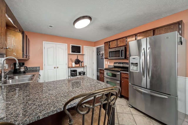 kitchen with kitchen peninsula, a textured ceiling, stainless steel appliances, sink, and light tile patterned flooring