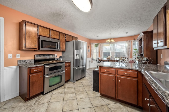 kitchen with sink, stainless steel appliances, decorative light fixtures, a textured ceiling, and light tile patterned floors