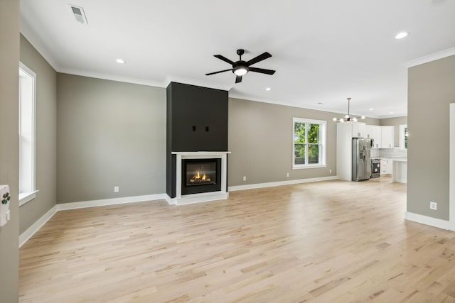 unfurnished living room with crown molding, a large fireplace, ceiling fan with notable chandelier, and light wood-type flooring