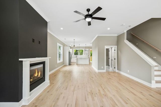 unfurnished living room with ceiling fan with notable chandelier, light hardwood / wood-style floors, and ornamental molding