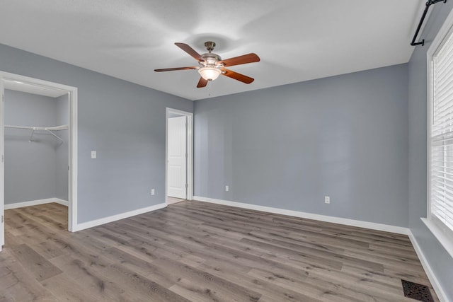 unfurnished bedroom with ceiling fan, multiple windows, light hardwood / wood-style floors, a walk in closet, and a closet