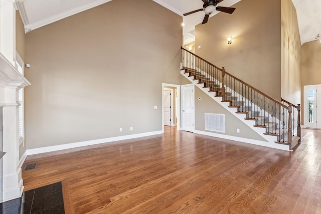 unfurnished living room featuring hardwood / wood-style floors, crown molding, ceiling fan, and a towering ceiling