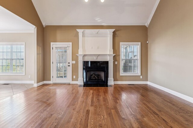 unfurnished living room with a tiled fireplace, wood-type flooring, ornamental molding, and vaulted ceiling