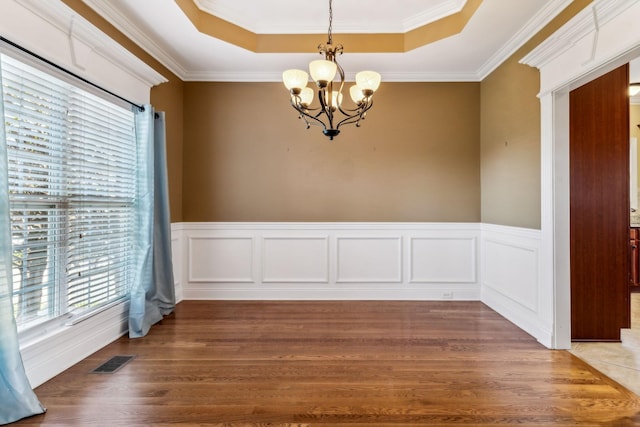 unfurnished dining area featuring crown molding, dark hardwood / wood-style floors, an inviting chandelier, and a tray ceiling