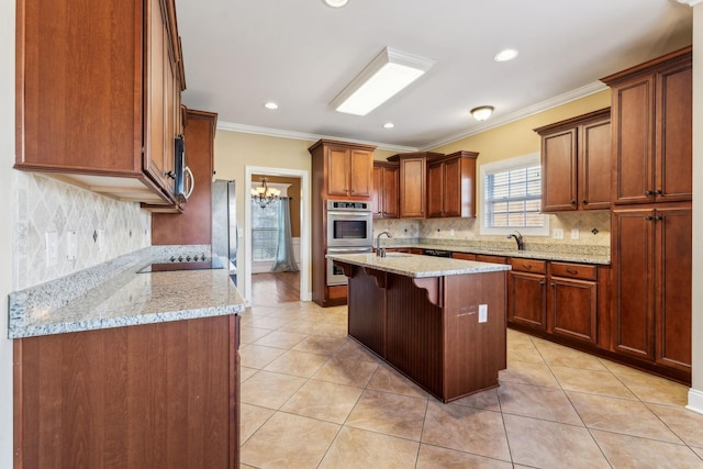 kitchen featuring appliances with stainless steel finishes, a kitchen bar, ornamental molding, a kitchen island with sink, and a notable chandelier